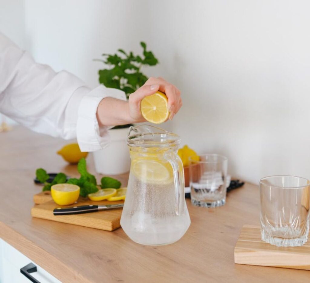 Adding fresh lemon juice to a homemade electrolyte drink recipe in a glass pitcher